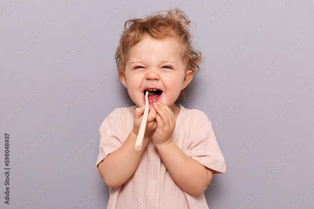 Oral hygiene. Dental care. Laughing funny little child baby brushing teeth isolated over gray background enjoying wearing t-shirt, free space for advertisement. Oral hygiene. Dental care. Laughing funny little child baby brushing teeth isolated over gray background enjoying wearing t-shirt, free space for advertisement.