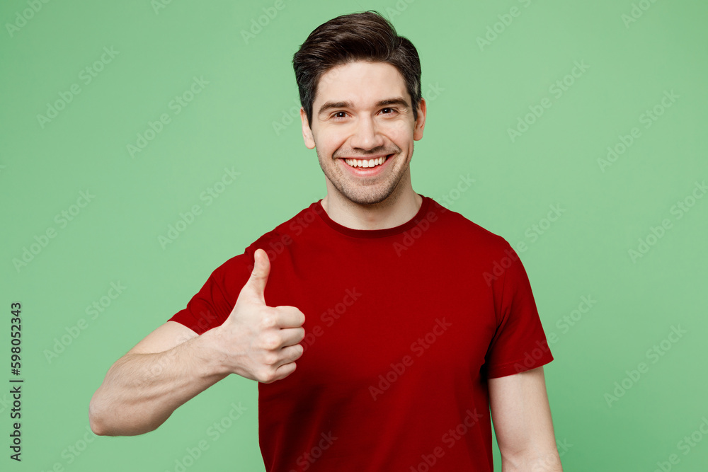 Young satisfied smiling happy brunet caucasian man he wears red t-shirt casual clothes showing thumb up like gesture isolated on plain pastel light green background studio portrait. Lifestyle concept. Young satisfied smiling happy brunet caucasian man he wears red t-shirt casual clothes showing thumb up like gesture isolated on plain pastel light green background studio portrait. Lifestyle concept.