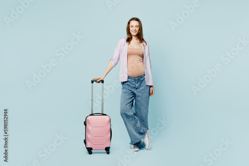 Full body young pregnant mom woman with belly tummy with baby wear casual clothes hold bag isolated on plain blue background. Tourist travel abroad in free time rest getaway. Air flight trip concept.