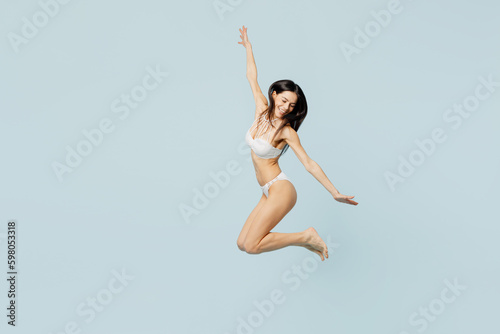 Full body side profile view young satisfied woman wear swimsuit jump high raise up hands near hotel pool isolated on plain pastel light blue cyan background. Summer vacation sea rest sun tan concept.