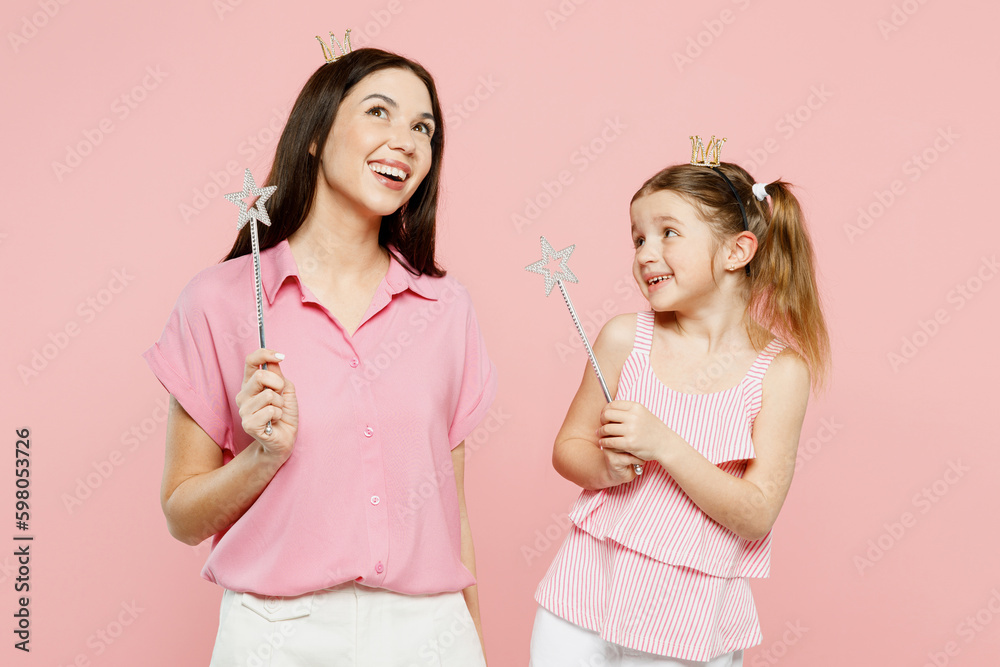 Happy woman wear casual clothes diadem princess crown with child kid girl 6-7 years old. Mother daughter hold magic wand fairy stick isolated on plain pastel pink background Family parent day concept Happy woman wear casual clothes diadem princess crown with child kid girl 6-7 years old. Mother daughter hold magic wand fairy stick isolated on plain pastel pink background Family parent day concept