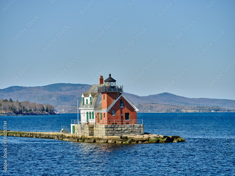 The Rockland Breakwater Lighthouse as seen from the ferry heading back into Rockland harbor with the town of Rockland maine in the background