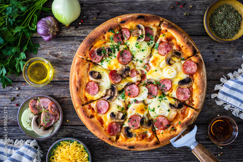 Circle pizza with sausages, onion and mozzarella cheese on wooden table 