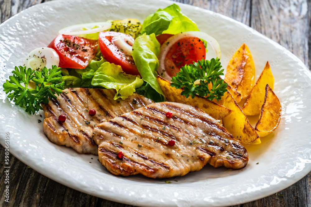 Barbecued pork chops with fried potatoes and fresh vegetables on wooden table
Barbecued pork chops with fried potatoes and fresh vegetables on wooden table