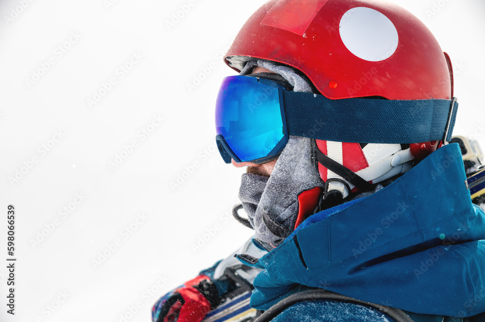 Naklejka premium sportsman in a helmet and goggles in profile against the background of white falling snow, looks to the side enjoying a beautiful view of the mountains