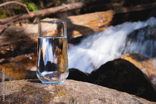 Natural drinking water in a glass glass on the background of the nature river. Sunlight reflects on the glass showing clear clear water.