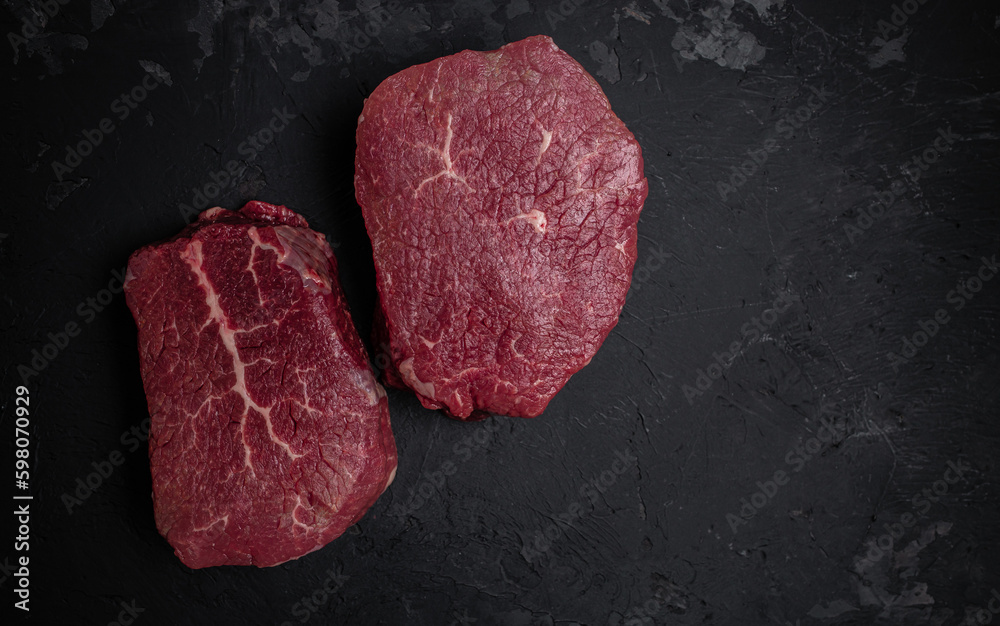 Two fresh raw beef steaks with spices ready to cook on a dark background. Culinary, cooking, concept. banner, menu, recipe place for text, top view