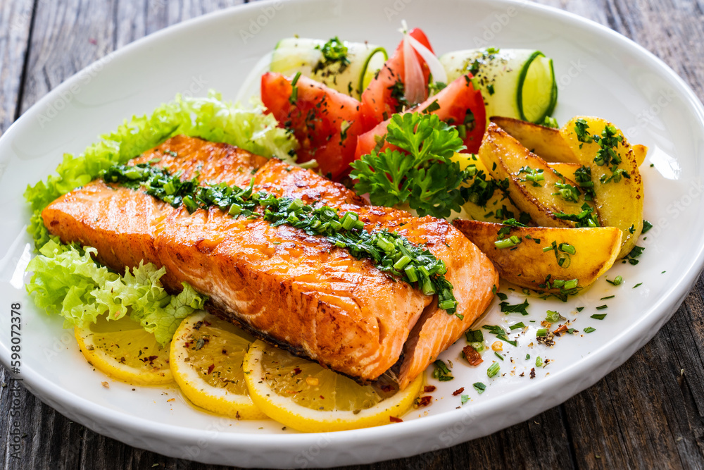 Seared salmon steak with fried potatoes and fresh vegetable salad served on wooden table
Seared salmon steak with fried potatoes and fresh vegetable salad served on wooden table
