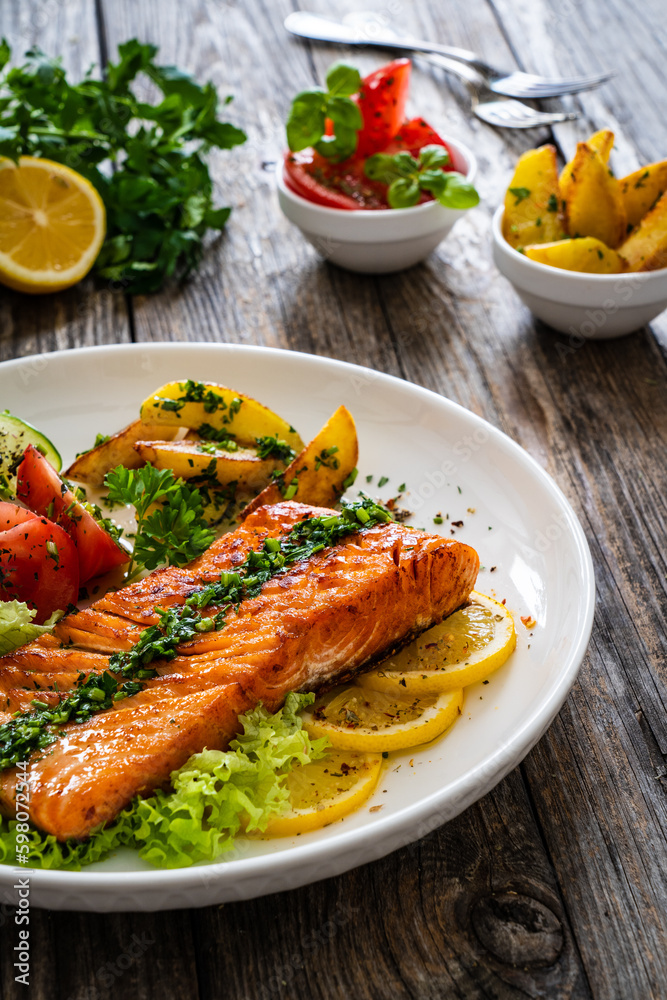Seared salmon steak with fried potatoes and fresh vegetable salad served on wooden table
Seared salmon steak with fried potatoes and fresh vegetable salad served on wooden table