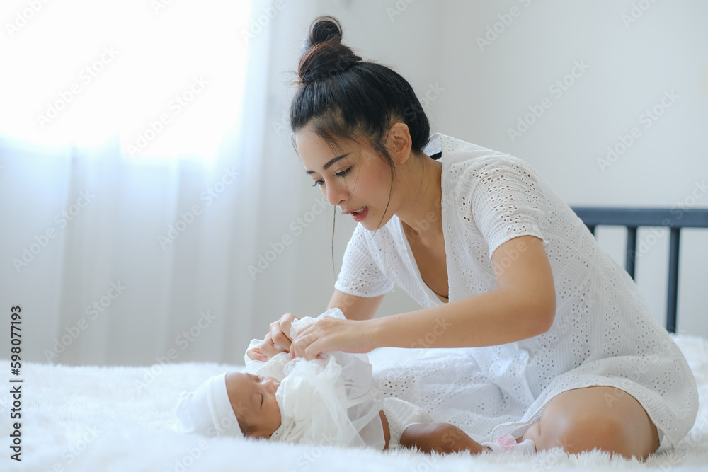 Mother change baby cloth carefully while infant are sleeping on white bed. Taking care, protection, bonding mother and kid concept. Mother change baby cloth carefully while infant are sleeping on white bed. Taking care, protection, bonding mother and kid concept.