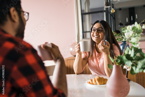 Young diverse loving couple eating croissant and talks together at home in breakfast time. Communication and relationship concept