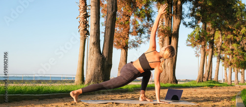 Fototapeta Naklejka Na Ścianę i Meble -  Fitness.Young woman teen fitness sport garden outdoors following guide outdoor online  trainer laptop.Wellness.Healthy lifestyle.Exercising home.Fitness online.Meditation,practicing,healthy lifestyle