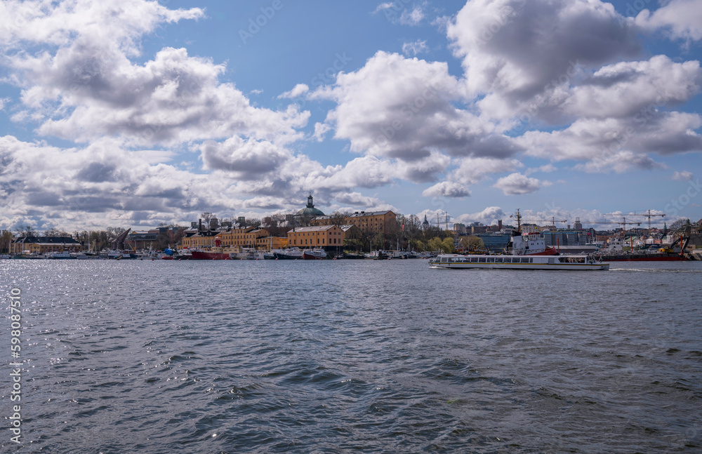Panorama over the ships and old maritime buildings on the island Skeppsholmen, tourist boat passing in the bay Nybroviken, a sunny spring day in Stockholm