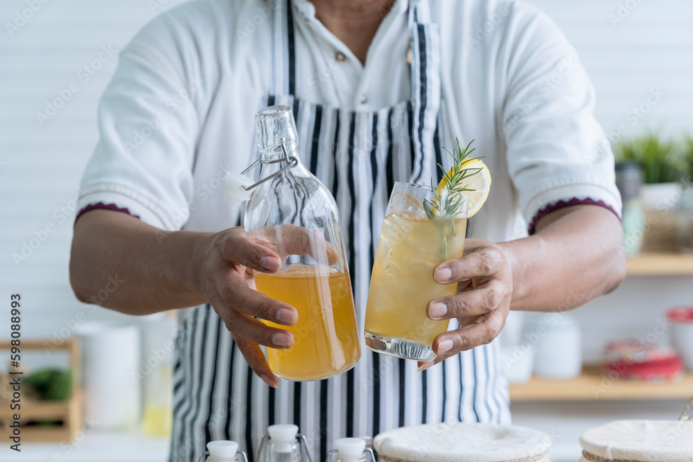 Man holding cup of kombucha tea. Kombucha tea with lemon and sweetened root filling in glass jug on kitchen background.