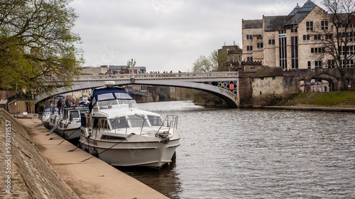 York England a bustling cityscape of tall buildings and a bridge, with a river below filled with boats and other modes of transportation. Above, clouds span the vast blue sky. photo