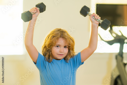Child workout kid in gym. Sport activities at leisure with children. Blonde boy holding dumbbells. Sports exercises for children. Funny child lifting the dumbbells.