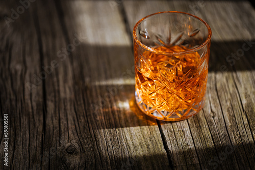 A glass of Whiskey on a rustic wooden board, that can be surface of barrel. Moody atmosphere.