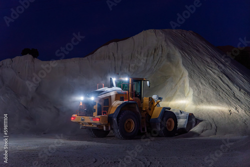 Heavy construction and mining machinery filling the bucket of a stockpile during the night shift.