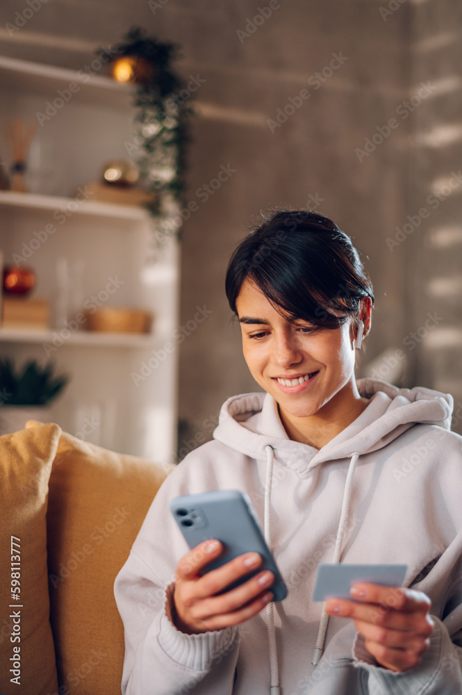 Woman using smartphone and holding credit card while online shopping from home Woman using smartphone and holding credit card while online shopping from home