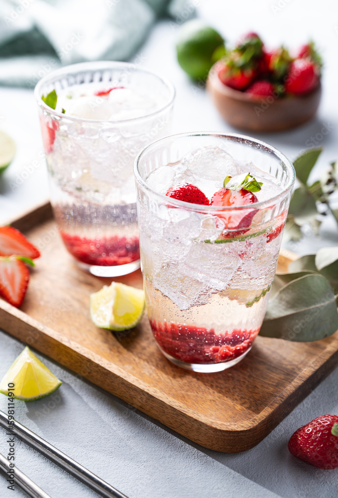 Fresh strawberry mojito in a glass with berries, lime, mint and ice in a wooden plate on a light background. The concept of a summer refreshing drink for a party Fresh strawberry mojito in a glass with berries, lime, mint and ice in a wooden plate on a light background. The concept of a summer refreshing drink for a party