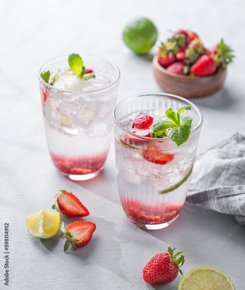 Fresh strawberry mojito in a glass with berries, lime, mint and ice on a light background with shadow. The concept of a summer refreshing drink for a party Fresh strawberry mojito in a glass with berries, lime, mint and ice on a light background with shadow. The concept of a summer refreshing drink for a party