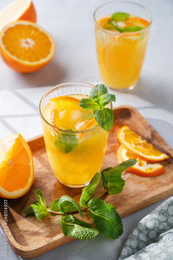 Freshly squeezed juice in a glass with fresh oranges, mint and ice on a light background with metallic tube and shadow. Freshly squeezed juice in a glass with fresh oranges, mint and ice on a light background with metallic tube and shadow.
