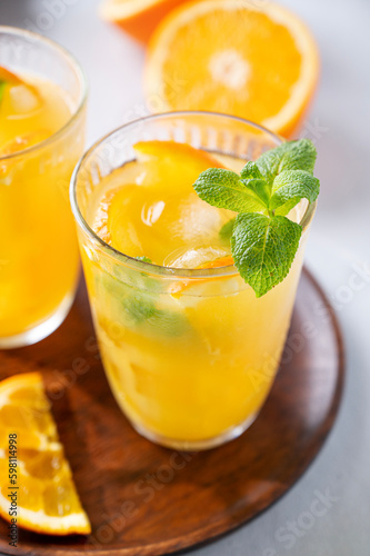 Freshly squeezed juice in a glass with fresh oranges, mint and ice on a light background close up. Healthy citrus detox drink for breakfast