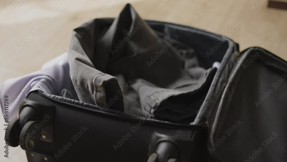 throws things in a suitcase. He is in a hurry to pack his luggage. Late