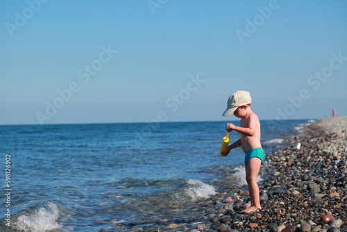 kid shoots from a water gun on the seashore . Pebble beach