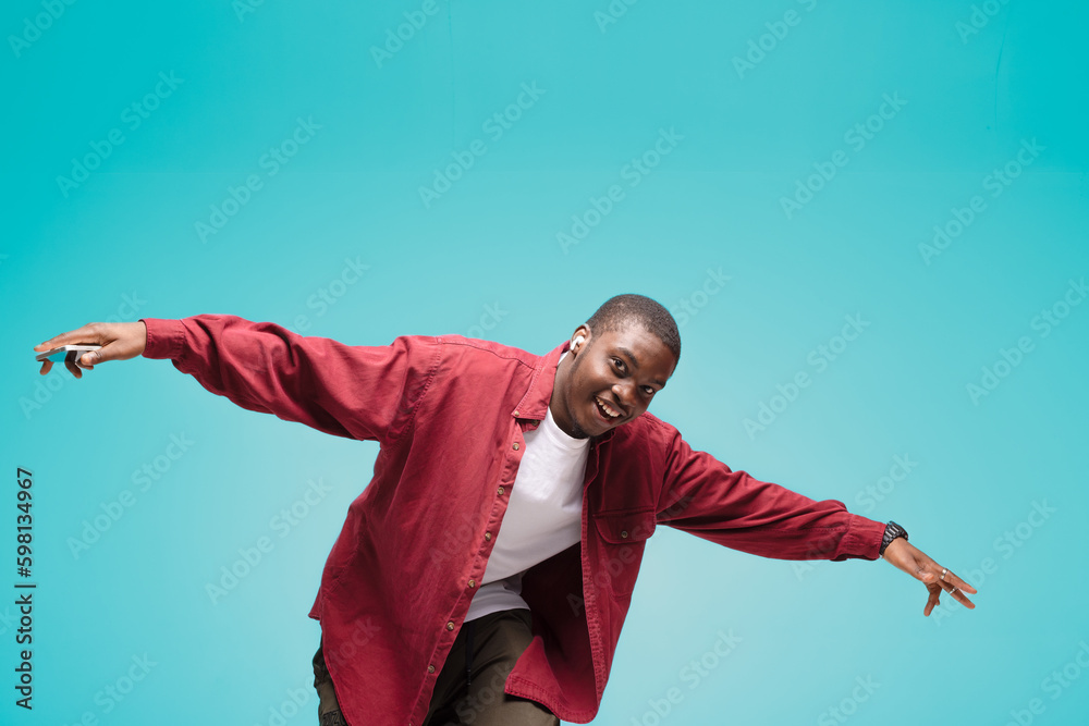 young African American man pictured isolated on gray background wearing casual clothes and hat dancing to music he is listening through wireless earphones, feeling relaxed and happy young African American man pictured isolated on gray background wearing casual clothes and hat dancing to music he is listening through wireless earphones, feeling relaxed and happy