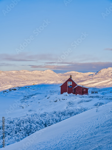 A red Norwegen wooden house covered in snow during a winter sunset in Eidfjord, Norway