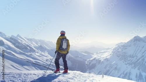 A skier arrives at the top of a snow-covered mountain and observes the  landscape, in the French Alps