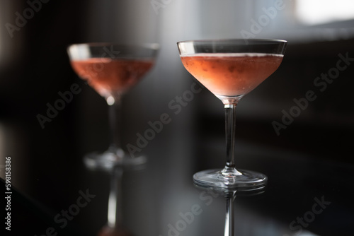 Two glasses of pink champagne on a glass table by a window at sunset