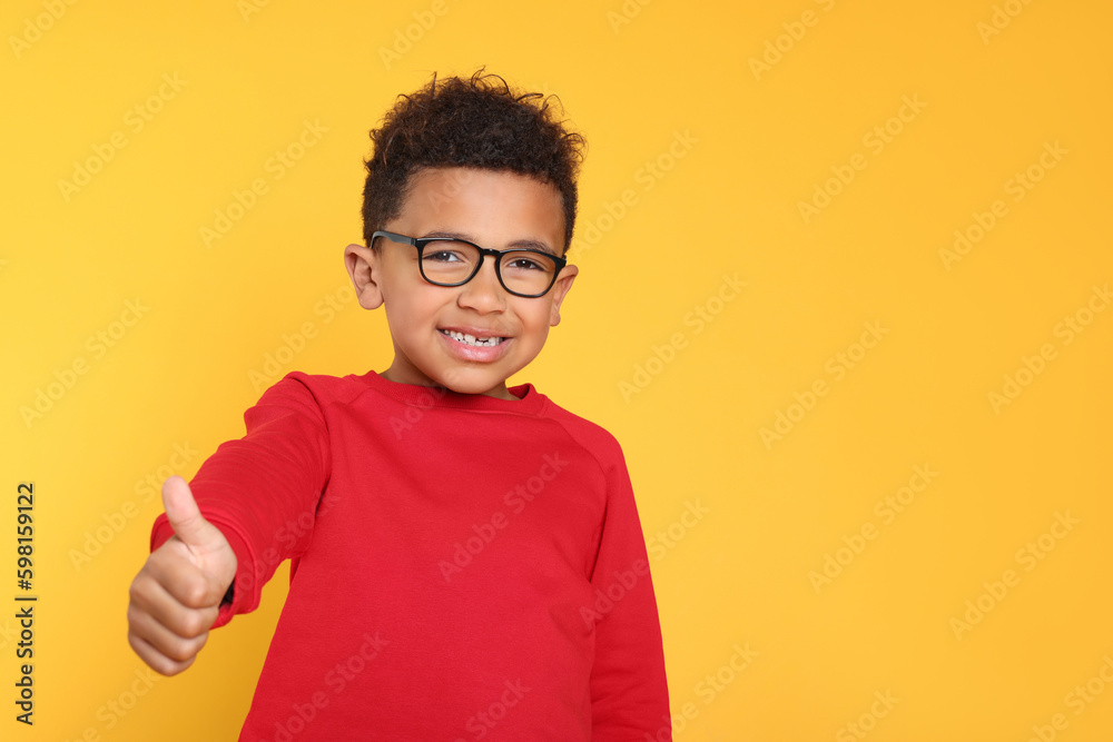 African-American boy with glasses showing thumb up on yellow background. Space for text African-American boy with glasses showing thumb up on yellow background. Space for text