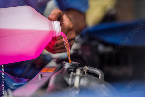 Auto mechanic pouring antifreeze engine coolant into car radiator fill hole ,engine cooling system maintenance.	