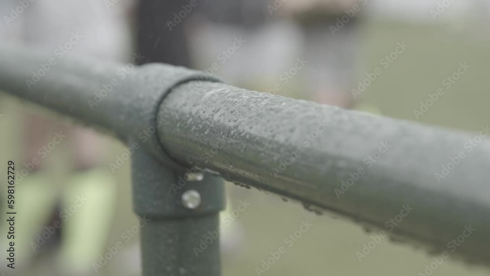Close up shot of a bar or fence covered in rain drops with footballers in the background in slowmotion LOG Close up shot of a bar or fence covered in rain drops with footballers in the background in slowmotion LOG