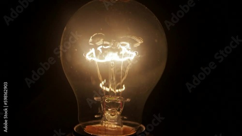 Close up of light bulb lighting up in the dark, thin metal filament sits in the middle of the bulb and shining periodically. Idea concept. photo