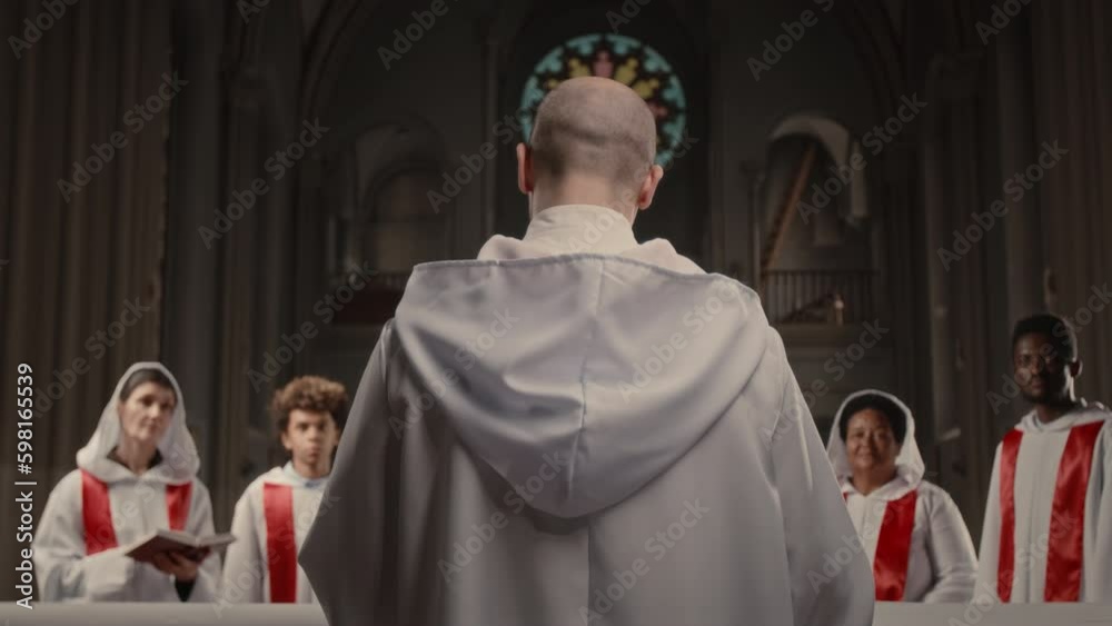 Back view of bald headed conductor speaking to multiethnic members of church choir while rehearsing for performance in old Catholic Church Back view of bald headed conductor speaking to multiethnic members of church choir while rehearsing for performance in old Catholic Church