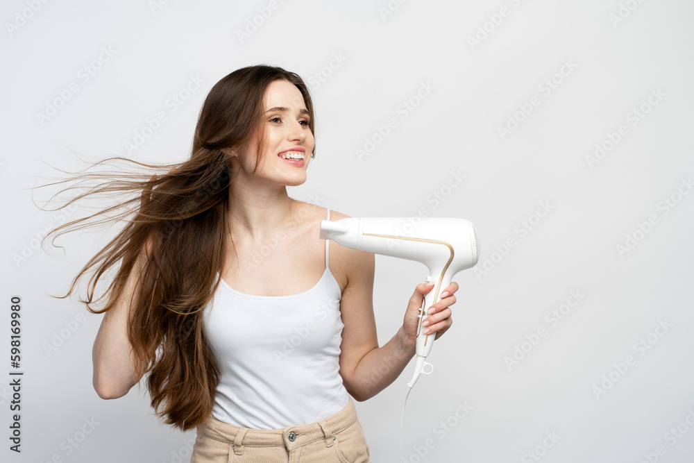 Portrait of beautiful smiling caucasian woman using hair dryer isolated on white background. Beauty, hair care, morning routine concept Portrait of beautiful smiling caucasian woman using hair dryer isolated on white background. Beauty, hair care, morning routine concept