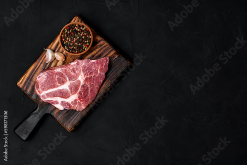 Raw pork steak on a wooden cutting board. Meat, dry pepper mixture, garlic on a black background. View from above.