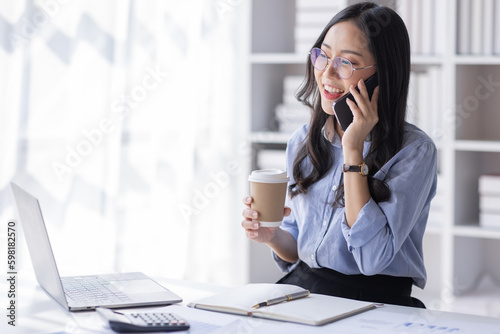 Cheerful business Asian woman freelancer making telephone call share good news about project working in office workplace, business finance concept.
