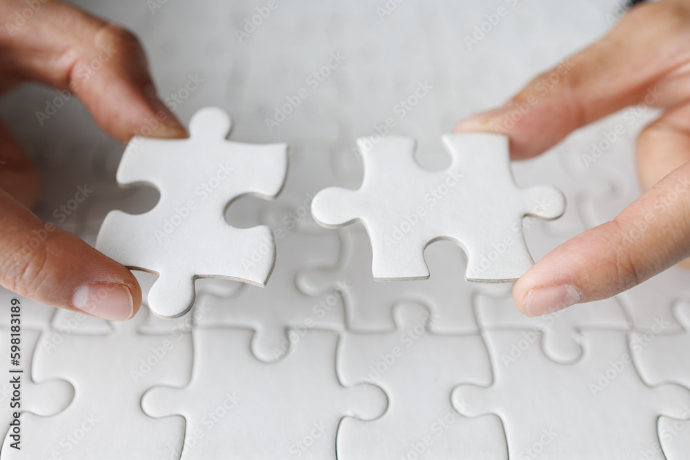 Business woman hand is trying to connect couple White jigsaw puzzle piece on a blue background. Symbol of association and connection. Concept of business strategy. Business woman hand is trying to connect couple White jigsaw puzzle piece on a blue background. Symbol of association and connection. Concept of business strategy.