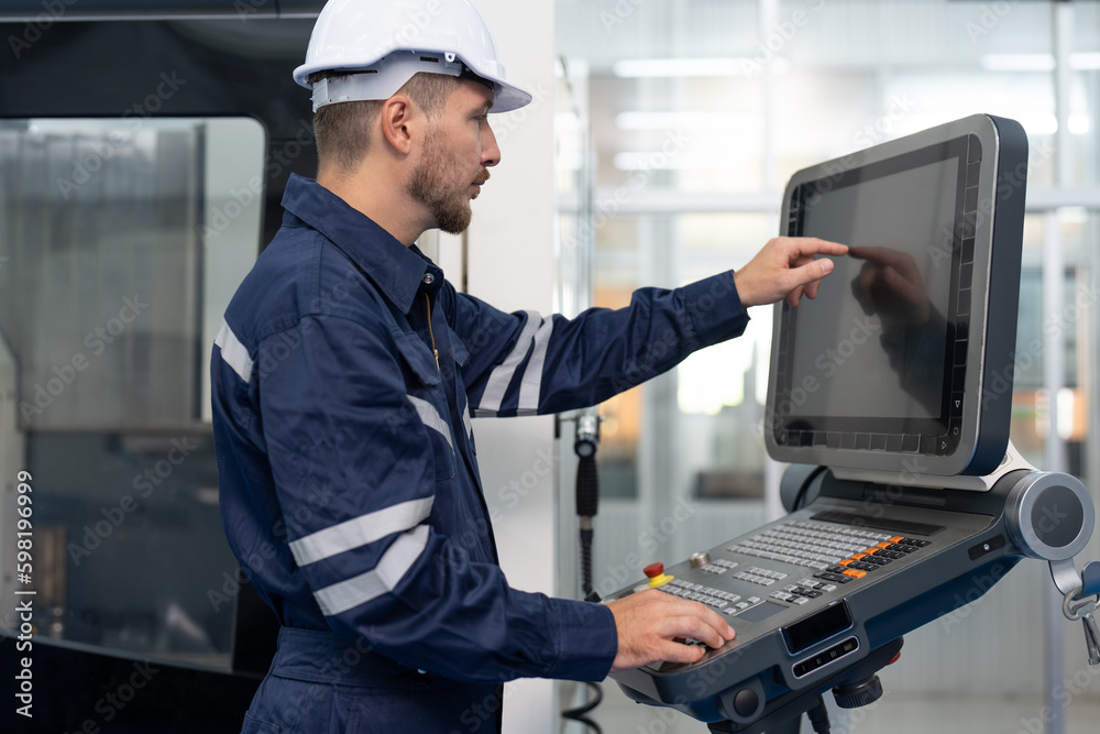 Male engineer operating cnc machine in control panel at factory. Smiling man technician in uniform and helmet safety working at workshop heavy metal industrial