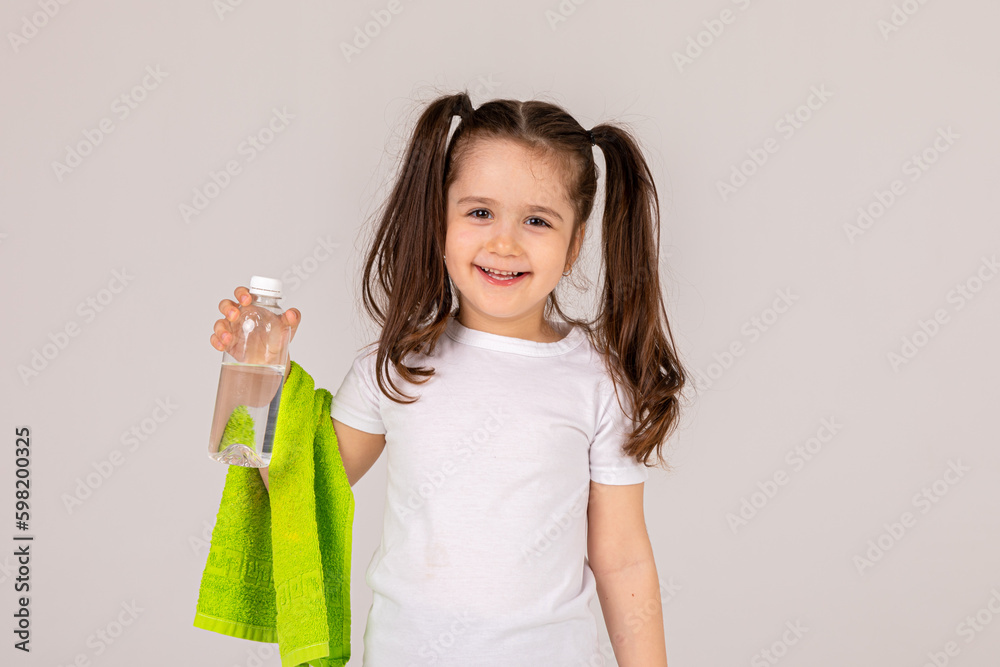 Studio fitness portrait isolated on white background. Image of a happy cheerful little sports girl osing isolated indoors drinking water with towel on a hand Studio fitness portrait isolated on white background. Image of a happy cheerful little sports girl osing isolated indoors drinking water with towel on a hand