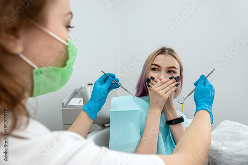 young female patient sits dentist closes her mouth from female dentist because she is afraid.