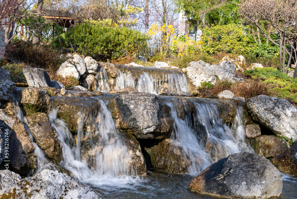 Fototapeta premium Little waterfall in Setagaya park, Vienna. View of waterfall in beautiful garden at springtime.