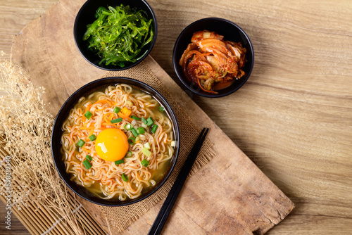 Asian instant noodle soup with fresh egg yolk eating with kimchi cabbage and seaweed salad, Table top view