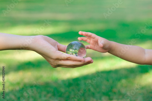 Fototapeta Naklejka Na Ścianę i Meble -  Adult person passes crystal ball to baby hand a healthy ecology to a new generation. Healthy ecology of the planet Earth. A healthy future for our generation. green glass background. Save the world.