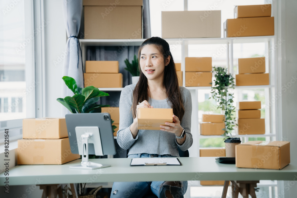 Shipping shopping online ,woman start up small business owner writing address on cardboard box at workplace.small business entrepreneur SME or freelance asian woman working with box at home. Shipping shopping online ,woman start up small business owner writing address on cardboard box at workplace.small business entrepreneur SME or freelance asian woman working with box at home.