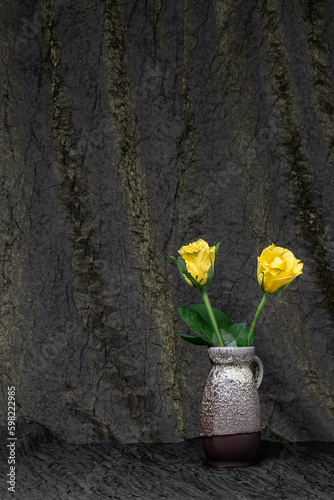 A beautiful bouquet of flowers of yellow roses in a gray vase on a background of dark brown fabric. Place for text, copy space